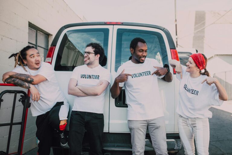 A diverse group of volunteers standing outside a van, smiling and socializing.