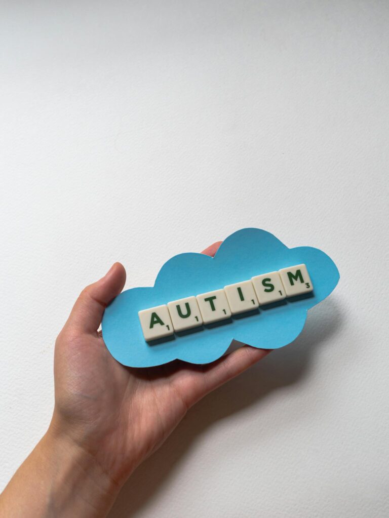 Close-up of a hand holding autism word tiles on blue cloud cutout.
